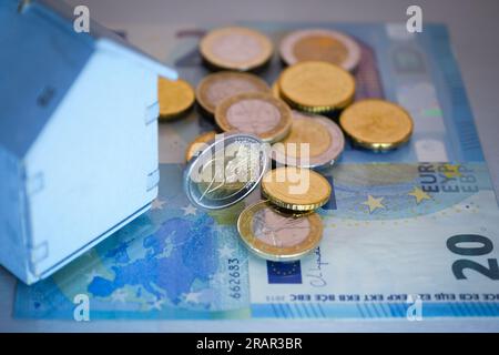 A small wooden house is placed on euro banknotes and nearby coins, concept of costs for the maintenance of the house, for the purchase, for the rent. Stock Photo