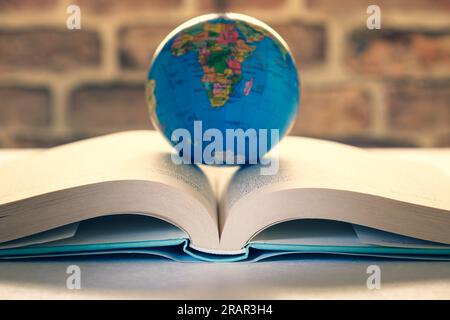 Hardcover book is open on a desk, globe placed in the center, "reading is like traveling" concept. Stock Photo