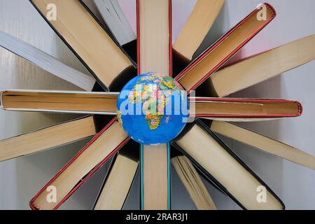 A globe rests on many books seen from above and positioned in a circle, the concept of "education for all" or "reading makes you travel". Stock Photo