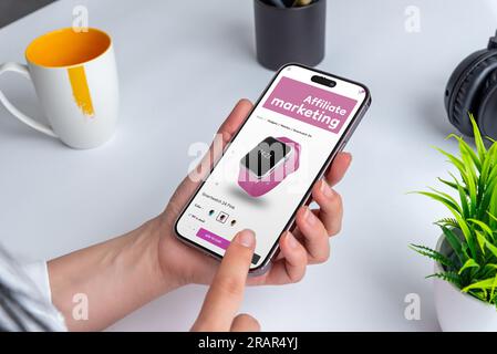 Ecommerce website offers affiliate marketing on smart phone display. Modern  web page with smart watch in woman hands Stock Photo