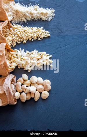 Natural almonds on a dark slate base. Almonds in different textures coming out of brown craft bags. Whole, sliced, diced or chopped and ground almonds Stock Photo