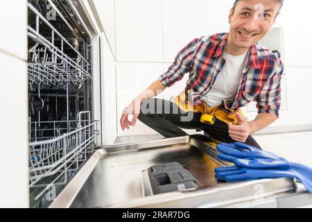 Worker using screwdriver to repair dishwasher at home stock photo Stock Photo