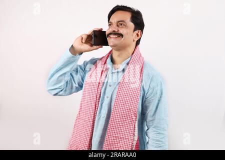 Portrait of an happy Indian bearded farmer man in rural India concept. Funky expressions white background. Cheerful farmer talking on a mobile phone Stock Photo
