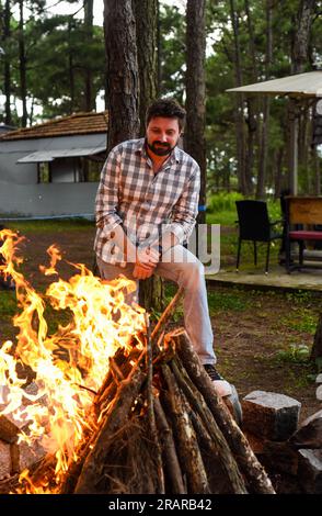 Bearded man making a bonfire in camping in the pine forest at night Stock Photo