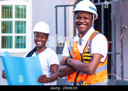 Male and female workers in hard hats standing in front of a building smiling Stock Photo