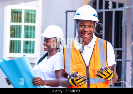 Male and female workers in hard hats standing in front of a building smiling Stock Photo