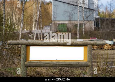 Empty white sign with wooden log frame. Industrial area on countryside Finland. Stock Photo