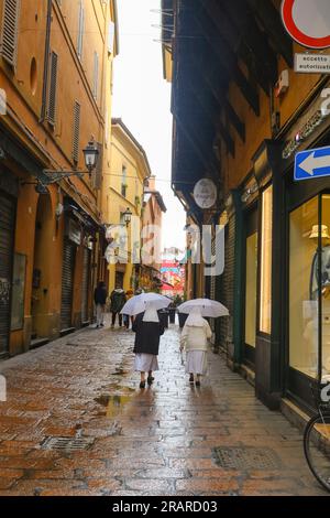 two nuns with white umbrellas walking on the narrow street of Bologna, Italy during rain Stock Photo
