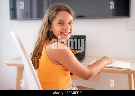 Head shot close up portrait of happy small pupil learning at home. Smiling little child girl enjoying doing lessons in living room. Smart kid schoolgi Stock Photo