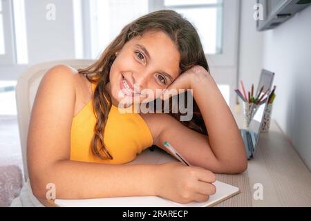 Head shot close up portrait of happy small pupil learning at home. Smiling little child girl enjoying doing lessons in living room. Smart kid schoolgi Stock Photo