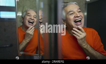 Happy senior man looking at himself in mirror reflection. Joyful emotion of elderly person laughing and smiling in morning ritual Stock Photo