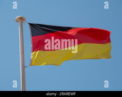 Germany the German national flag waving in the wind on a flagpole with blue sky background. Stock Photo