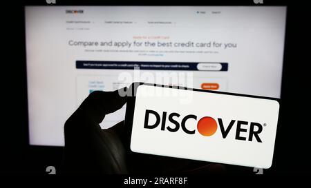 Person holding cellphone with logo of US company Discover Financial Services on screen in front of business webpage. Focus on phone display. Stock Photo