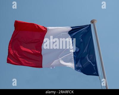 French national flag waving on a flagpole against a bright blue sky ...
