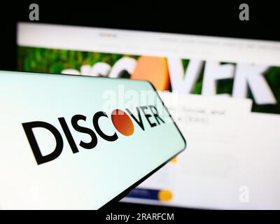 Mobile phone with logo of American company Discover Financial Services on screen in front of website. Focus on center-left of phone display. Stock Photo
