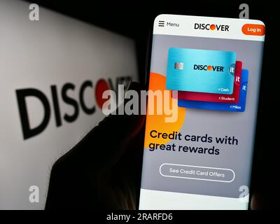Person holding cellphone with website of US company Discover Financial Services on screen in front of logo. Focus on center of phone display. Stock Photo
