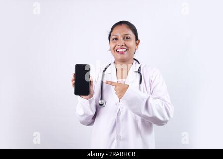 Beautiful portrait of a happy Indian female Doctor in uniform wearing stethoscope showing phone screen in hand. Stock Photo