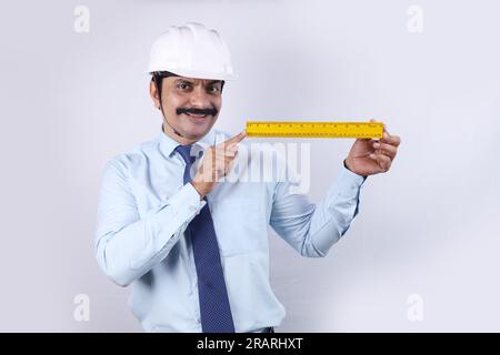 Happy Indian Construction worker doing engineer concept for future. The cheerful engineer is wearing engineering helmet. Holding measuring scale. Stock Photo