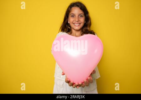 cheerful cute little lady receive birthday present hold heart shaped balloon isolated on yellow color background Stock Photo