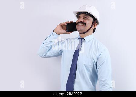 Happy Indian Construction worker doing engineer concept for a better future. The cheerful engineer is wearing an engineering helmet. talking on phone. Stock Photo