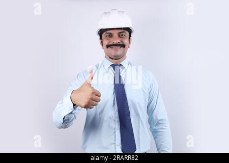 Happy Indian Construction worker doing engineer concept for a better future. The cheerful engineer is wearing an engineering helmet and showing mobil Stock Photo