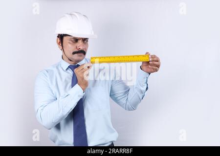 Happy Indian Construction worker doing engineer concept for future. The cheerful engineer is wearing engineering helmet. Holding measuring scale. Stock Photo