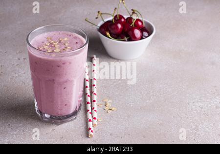 Milkshake with cherries, yogurt and oatmeal, drinking straws, bowl with fresh cherries on a beige textured background Stock Photo