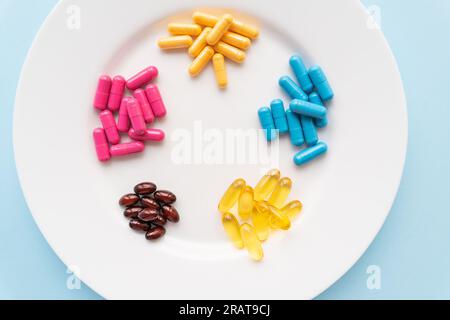 Food supplements of bright color lie on a white plate on a blue background. Concept of health support and lack of vitamins Stock Photo
