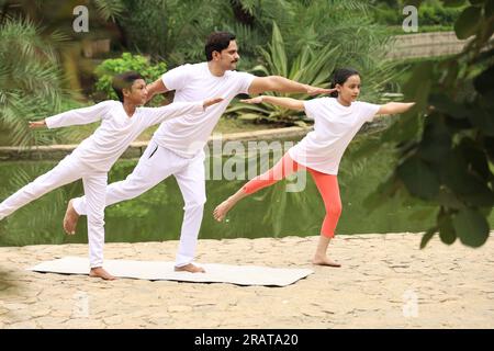 Trainer exercising and teaching kids the yoga poses in green environment early morning in park to maintain healthy lifestyle. International yoga day. Stock Photo