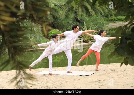 Trainer exercising and teaching kids the yoga poses in green environment early morning in park to maintain healthy lifestyle. International yoga day. Stock Photo