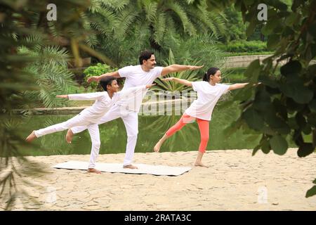 Trainer exercising and teaching kids the yoga poses in green environment early morning in park to maintain healthy lifestyle. International yoga day. Stock Photo