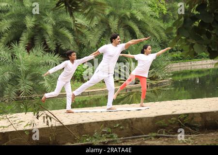 Trainer exercising and teaching kids the yoga poses in green environment early morning in park to maintain healthy lifestyle. International yoga day. Stock Photo