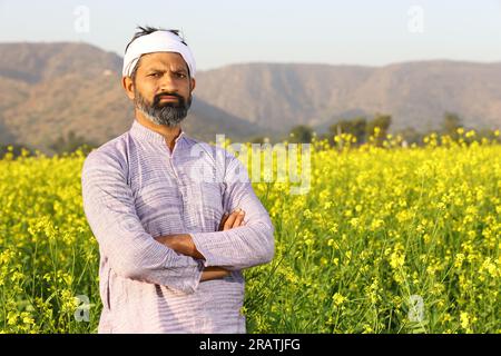 Farmer feeling proud of his effort that he did for growth of his field. Beautiful portrait of Indian rural happy farmer standing in mustard field. Stock Photo