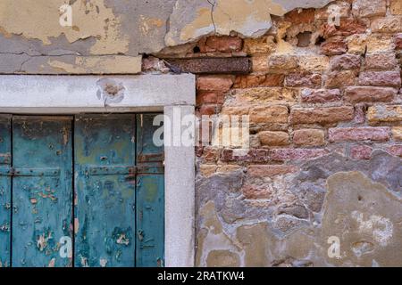 Detail with a green wooden shutter window on a worn out plastered red brick wall, in Venice Italy. Stock Photo