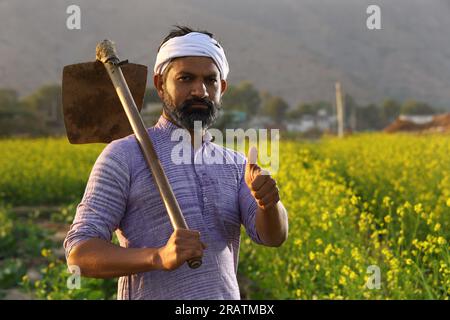 Angry bearded Indian farmer in turban standing with a shovel in his hand wearing Kurta pyjama. Stock Photo