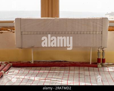 Installing water radiator in front of window in unfinished apartment Stock Photo