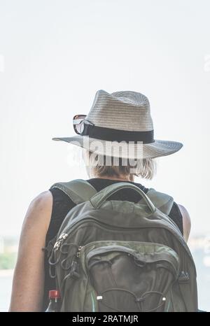 Rear view with a female explorer traveller with a backpack and wearing a hat.. Tourism hiking concept Stock Photo