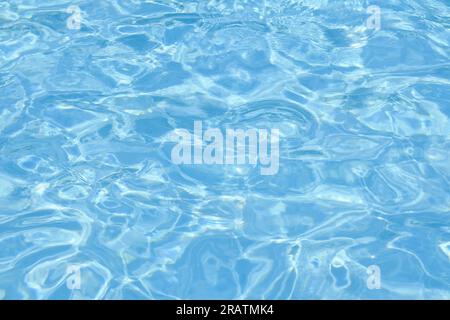 Defocused blurred transparent blue colored clear calm water surface texture with ripple. Shining blue water background. Water in swimming pool. Stock Photo