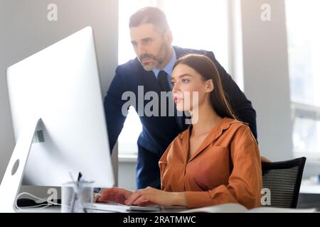Focused employees young woman and middle aged man looking at computer, working on project together in office Stock Photo
