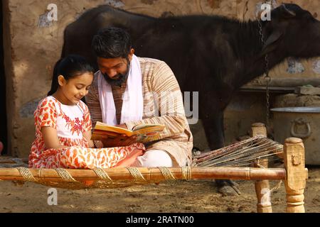Rural Indian father and daughter studying book together. Child education reaching all villages of India. Farmers are aware of teaching their daughter. Stock Photo