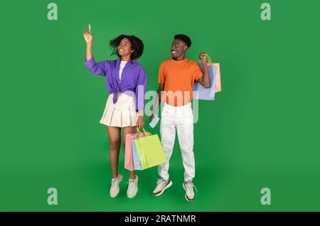 Smiling young african american guy and woman shopaholics with bags of purchases jumps, freeze in air Stock Photo