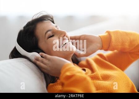 Closeup eastern woman reclining on couch, listening to music Stock Photo