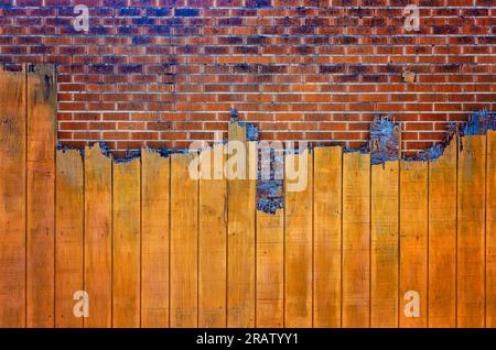 A brick wall is partially obscured by broken wooden boards, June 24, 2023, in Moss Point, Mississippi. The rough texture provides a rustic look. Stock Photo