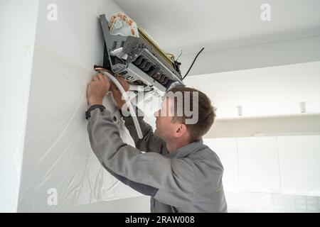 Installing air conditioner in house. Man specialist wearing work uniform fixing air cooler system. Stock Photo
