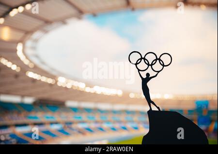 PARIS, FRANCE, JULY 7, 2023: Embodying Olympic Spirit: Statue of Athlete Holds Olympic Circle High at Modern Olympic Stadium. Capturing the Essence of Stock Photo