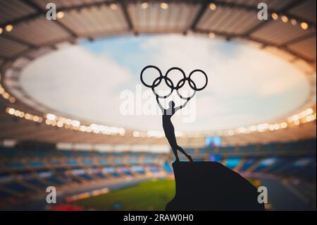 PARIS, FRANCE, JULY 7, 2023: Embodying Olympic Spirit: Statue of Athlete Holds Olympic Circle High at Modern Olympic Stadium. Capturing the Essence of Stock Photo