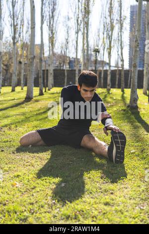 Sporty handsome man stretching legs after working out in city public park Stock Photo