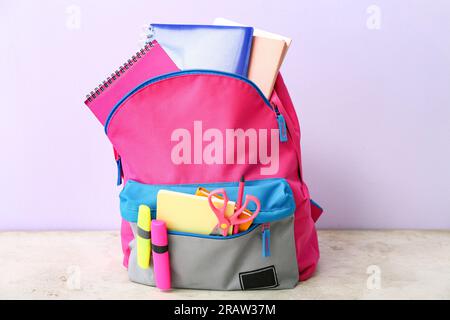 Color school backpack with notebooks, markers and scissors on light grunge table near lilac wall Stock Photo