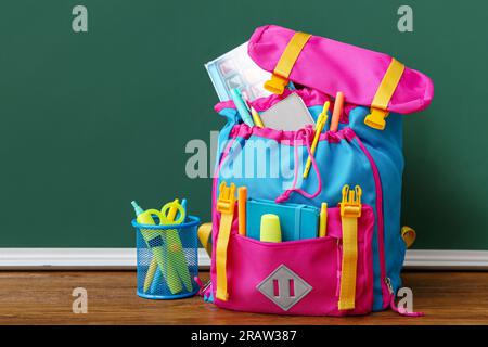Color school backpack with markers, pens and watercolor on brown wooden table near chalkboard Stock Photo