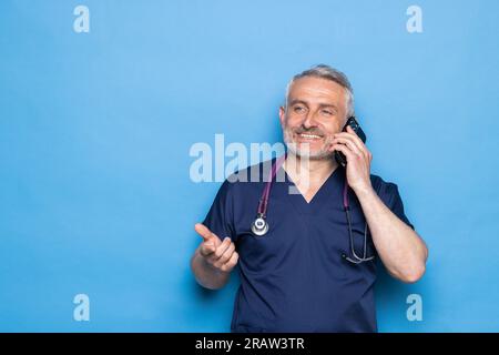 Doctor patient communication. Cheerful handsome gtey-haired mature doctor wearing white medical coat and eyeglasses using cell phone, calling patient Stock Photo